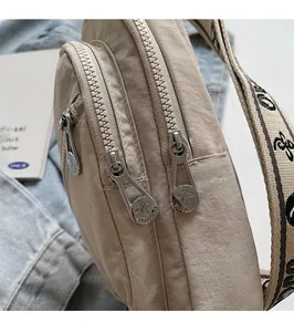 Detail of smooth silver dual metal zippers on a beige nylon crossbody bag with woven strap