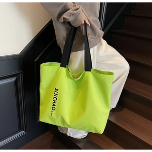 Detail of large neon green tote bag with wide black strap and chic graphic letter print