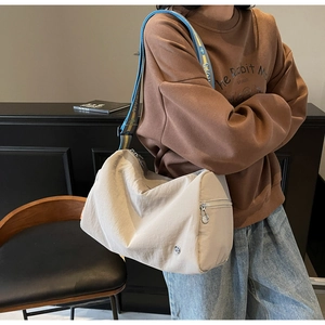 Detail of crossbody bag with a blue and yellow wide shoulder strap on a beige fabric