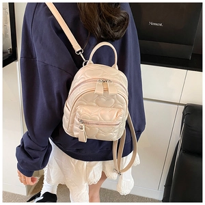 Detailed view of beige mini backpack with heart quilted stitching worn by model