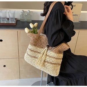 Macro detail of gradient woven straw texture and tassel charm on a large shoulder tote bag