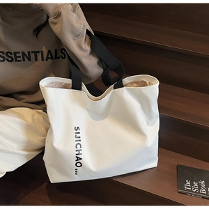 Detail of a large white canvas tote bag with black letter print shown in a lifestyle setting