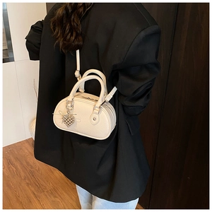 Détail du sac boston en cuir grainé blanc cassé avec breloque raisin et bandoulière