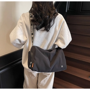 Detail of a casual black nylon crossbody bag featuring a branded wide woven shoulder strap