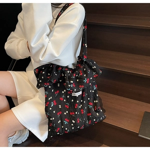Detail of black tote bag with red cherry print, ruffled edges and Magic pocket label
