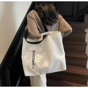Detail of white nylon tote bag showing black letter print and durable strap handle