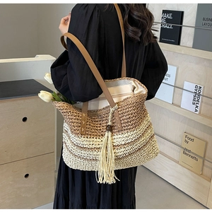 Detail of woven gradient tote bag featuring brown leather straps and long tassel ornament