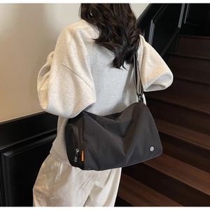 Detail of a black nylon crossbody bag with side zipper pocket and logo on model