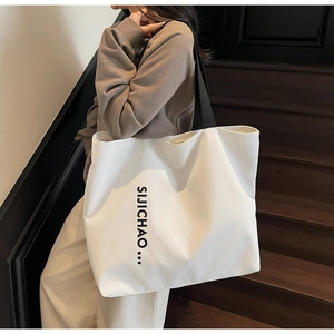 Detail view of large white canvas tote bag with black letter print and wide strap