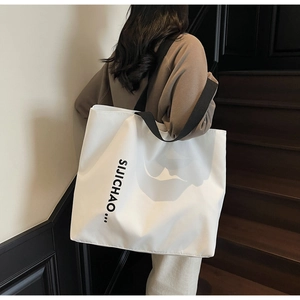 Detailed back view of a large white tote bag with black straps and letter print