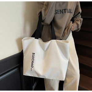 Detail of white nylon tote bag with wide black straps shown in a lifestyle daily setting