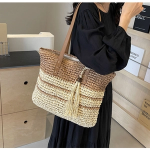 Detail shot of a large woven tote bag with a brown leather strap and long fringe tassel