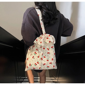 Detail of white canvas shoulder bag featuring red cherry prints and ruffled edges