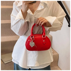Détail du sac polochon en cuir rouge avec un charm de perles métalliques en cœur