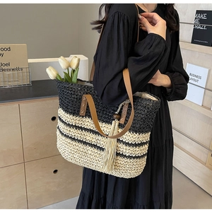 Detail of woven tote bag with stripe pattern, brown leather handle, and stylish fringe tassel