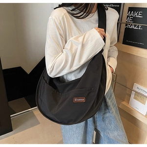 Model wearing a large black nylon crescent crossbody bag with a brown leather logo tag