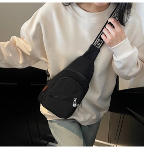 Detail of black nylon crossbody bag with printed SJC strap and orange woven label on model