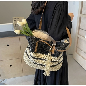 Detail of woven straw tote bag featuring black stripes, leather handles, and long tassel