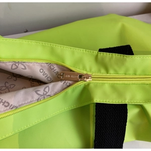 Detail of neon green nylon tote showing metal zipper and patterned logo lining