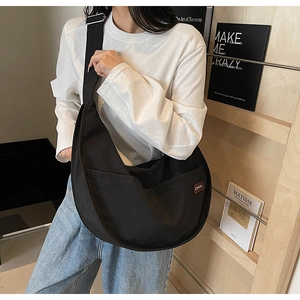 Side view of black nylon crescent tote bag with adjustable strap and logo detail