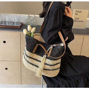 Detail of woven straw tote bag with black stripes and brown leather tassel charm