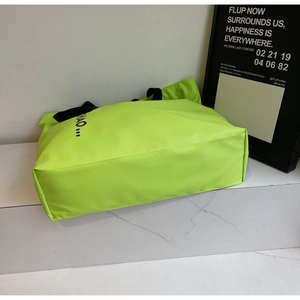 Detail of neon green nylon tote bag featuring wide black canvas handles on marble surface