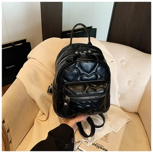 Detail of heart-quilted black leather mini backpack on a cozy neutral chair