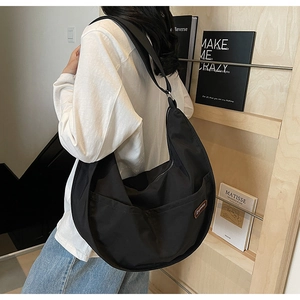 Detail view of large black nylon crescent bag with side pocket and brown brand patch