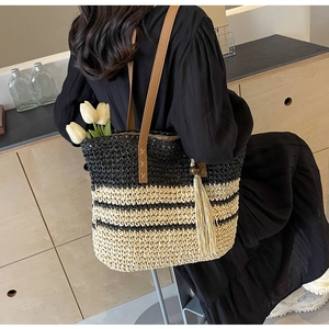 Close-up of woven tote bag with stripe pattern, leather handle and tassel detail
