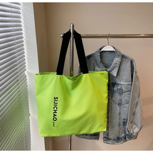 Detail of neon green nylon tote bag with black letter print hanging on a metal rack