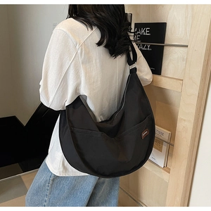 Detailed side view of black nylon half-moon crossbody bag with silver buckle and brand label