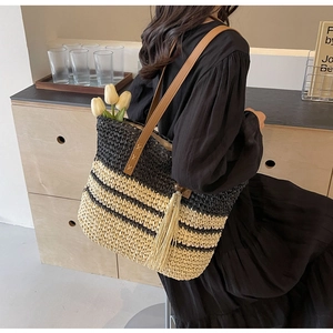 Detail of woven straw tote bag with black and white stripes and brown leather strap