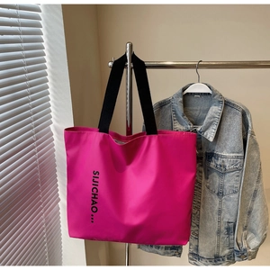 Detail of rose red nylon tote bag with black letter print and canvas handles on a hanger