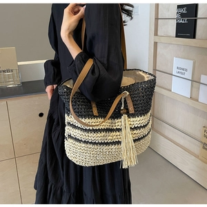 Detail of woven straw tote bag featuring black and yellow stripes with fringe tassel