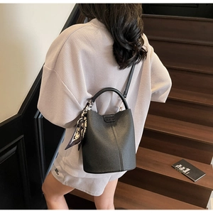 Gros plan d'un sac seau noir en cuir grainé avec un foulard décoratif sur la poignée