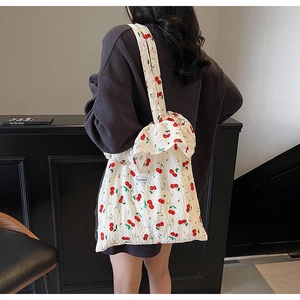 Detail of white cherry print tote bag with ruffled edges worn on a shoulder