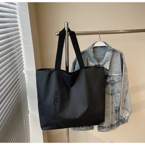 Detail of a large black tote bag featuring a logo, hanging in a bright stylish interior