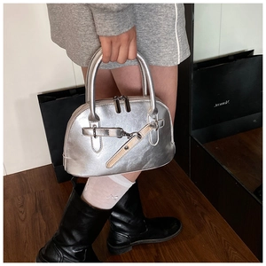 Detail of silver metallic handbag with decorative belt and dual metal zippers