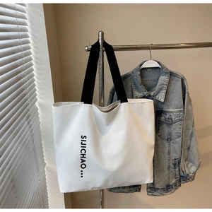 Close-up of a white canvas tote bag with black letter print and casual woven handles