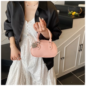 Mini sac à main rose en cuir grainé avec pendentif boule argentée porté par un modèle