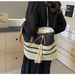 Detail of striped straw tote bag featuring a leather strap and beige tassel charm
