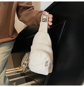 Detail view of cream nylon chest bag with triple zippers and logo patterned strap