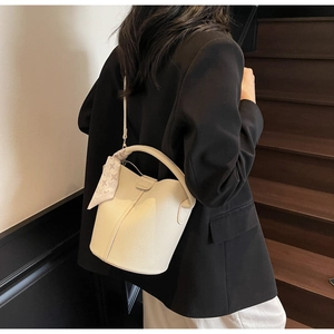 Détail d'un sac seau en cuir grainé avec foulard en soie sur un escalier en bois