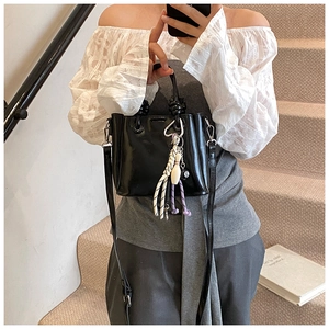 Detail of black glossy bucket bag with trendy charms and adjustable shoulder strap