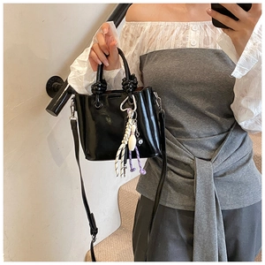 Detail of glossy black bucket bag featuring knotted handles and sporty rope pendant