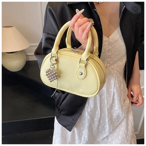 Détail du sac à main en cuir grainé jaune clair avec breloque cœur argentée et poignées