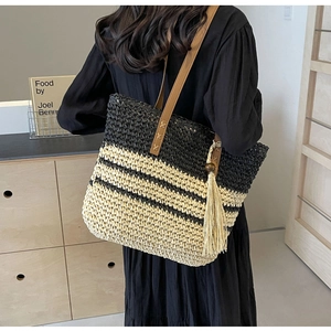 Detail of striped straw tote with leather straps and wooden bead tassels on model