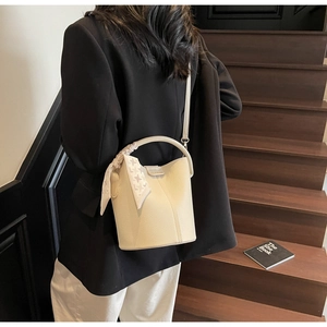 Gros plan du sac seau crème avec texture litchi et foulard en soie sur un mannequin