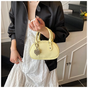 Gros plan d'un sac à main jaune pâle en cuir grainé avec breloque cœur et zip argenté