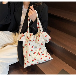 Detail of white cotton tote bag with red cherry prints and decorative ruffled edge trim